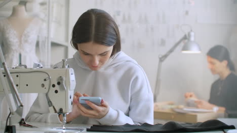 Woman-seamstress-looks-at-the-smartphone-screen-in-the-workplace.-Write-text-messages-to-customers.